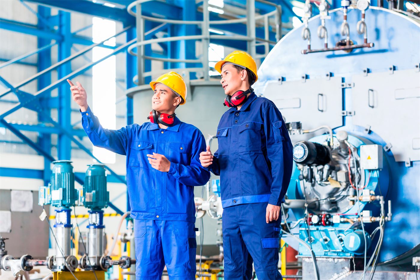 Técnicos con casco y protección auditiva supervisando una planta industrial